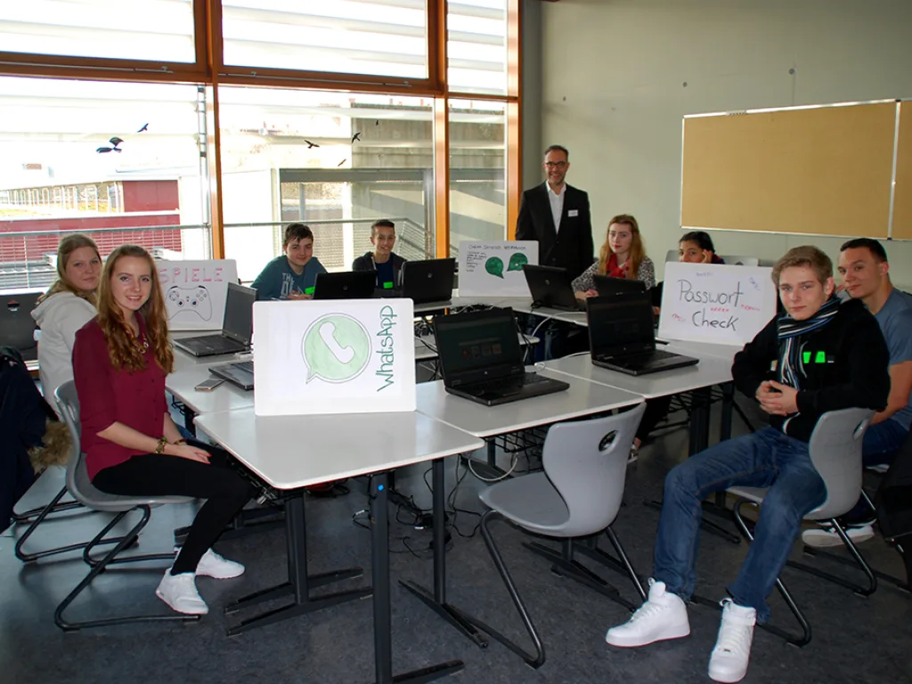 Jugendliche sitzen an Laptops vor einer Stellwand zum Thema Internet.